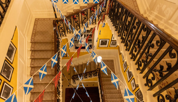 A high-angle, top-down view of a grand multi-story staircase decorated with crisscrossing Scottish saltire and red tartan bunting.